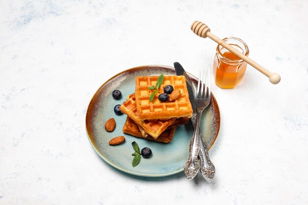 Free Photo traditional belgian waffles with fresh berries and honey on grey concrete surface. 