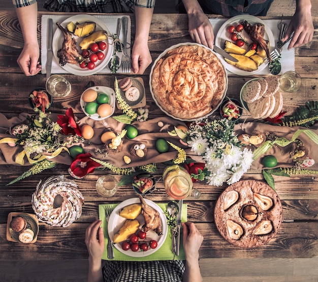 Free Photo traditional easter celebration, easter holiday party. holiday friends or family at the festive table with rabbit meat, vegetables, pies, eggs, top view. friends hands eating and drinking together.