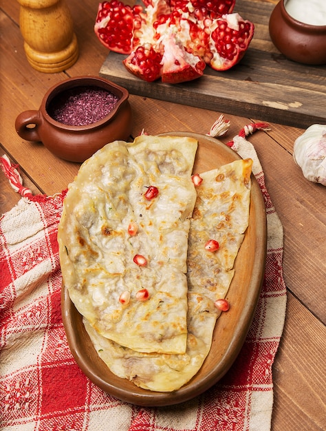 Traditional meat vegetable gutab, qutab, gozleme on wooden board with sumakh and pomegranate seeds