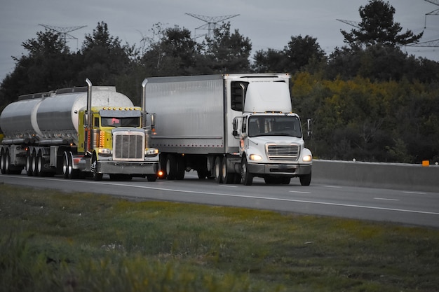 Trailer trucks driving on the road surrounded by beautiful green trees