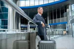 Free photo tranquil pensive businessman with the suitcase standing at airport terminal