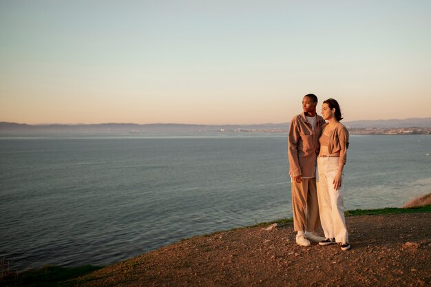 Trans couple holding each other on the beach while watching the sunset