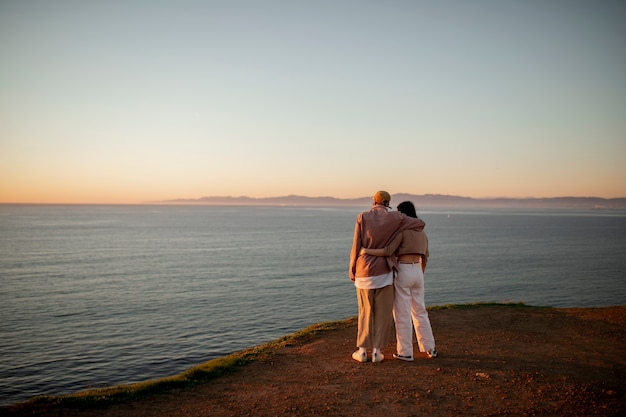 Free photo trans couple watching the sunset on the beach and holding each other