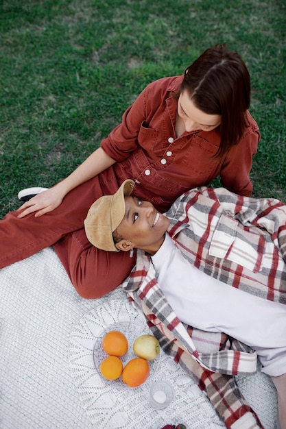 Trans man keeping his head on his girlfriend lap while having a picnic at the park