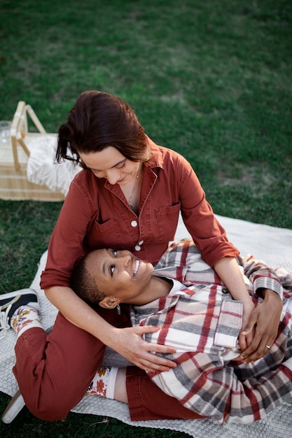 Trans man smiling and keeping his head on his girlfriend lap while having a picnic at the park