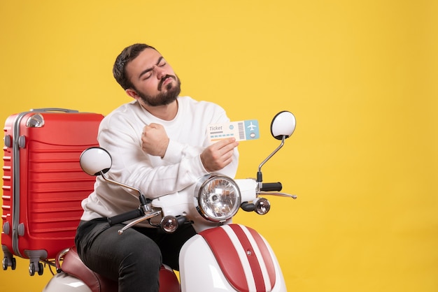 Travel concept with ambitious man sitting on motorcycle with suitcase on it showing ticket on yellow