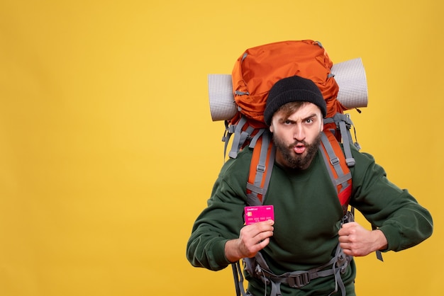 Free photo travel concept with ambitious young guy with packpack and holding bank card on yellow