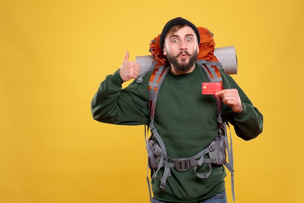 Free photo travel concept with confident young guy with packpack and holding bank card making ok gesture on yellow