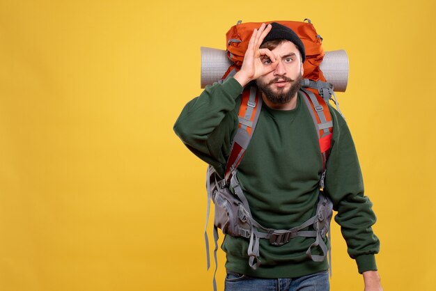 Free photo travel concept with focused young guy with packpack and making eyeglasses gesture on yellow