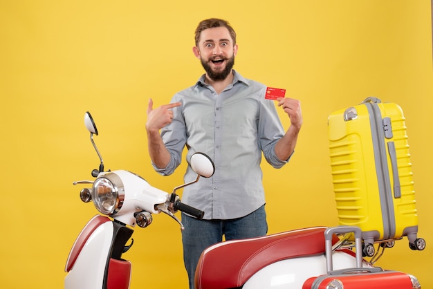 Free photo travel concept with smiling young man standing behind motocycle with suitcases on it pointing bank card on yellow