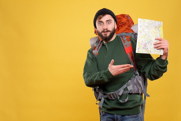 Travel concept with wondering young guy with packpack and holding map on yellow 