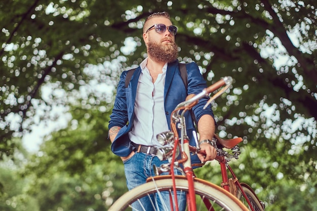 Free photo a traveler dressed in casual clothes and sunglasses with a backpack, relaxing in a city park after riding on a retro bicycle.