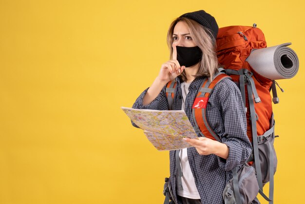 traveler girl with black mask and backpack holding map making hush sign