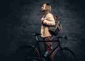 Free photo a traveler hipster man with long blond hair, wearing yellow jacket posing with authentic single speed bicycle.