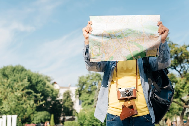 Free Photo traveler man holding map in front of his face with carrying backpack and camera