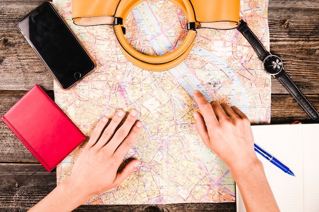 Free photo traveler's hand pointing at location on map with handbag and smartphone on table