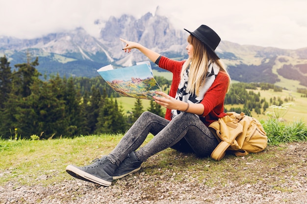 Traveler young woman with backpack and hat sitting on grass  and searching right direction on map