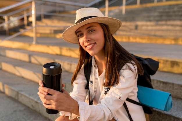 Free photo traveling woman with backpack and hat holding thermos