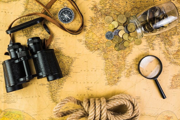 Travelling equipments and glass jar with coins on vintage map