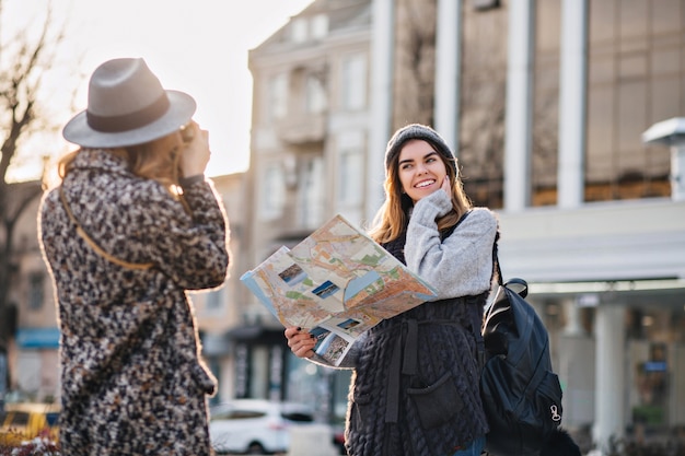 Free Photo travelling in sunny big city of fashionable joyful gilrs. taking photo, enjoying vacation, travel with backpack, citymap. showing true positive happy emotions, stylish look, posing to camera.