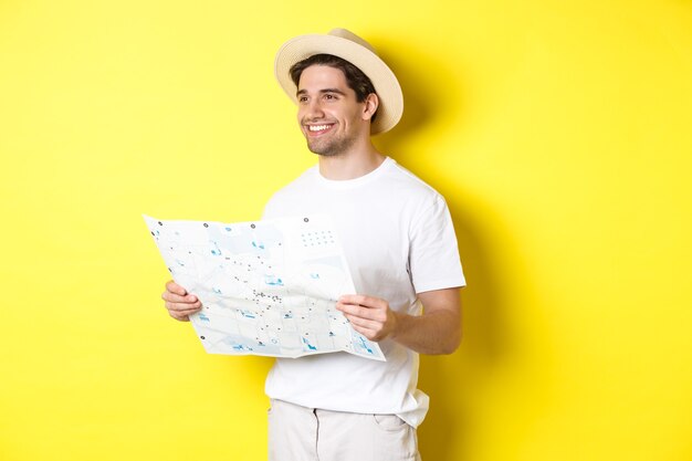 Travelling, vacation and tourism concept. Handsome guy tourist going sightseeing, holding map and smiling, standing over yellow background