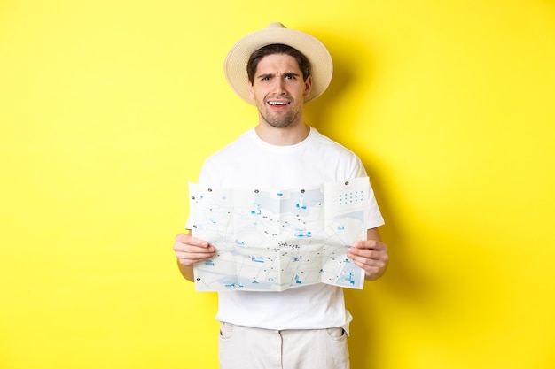 Free photo travelling, vacation and tourism concept. puzzled guy tourist cant understand map, looking confused at camera, standing against yellow background