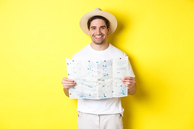 Free photo travelling, vacation and tourism concept. smiling young man going on trip, holding road map and smiling, standing over yellow background.