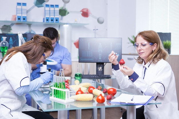 Free photo treatment study on genetically engineered strawberries in laboratory by group of scientist. test tubes with green solutions.