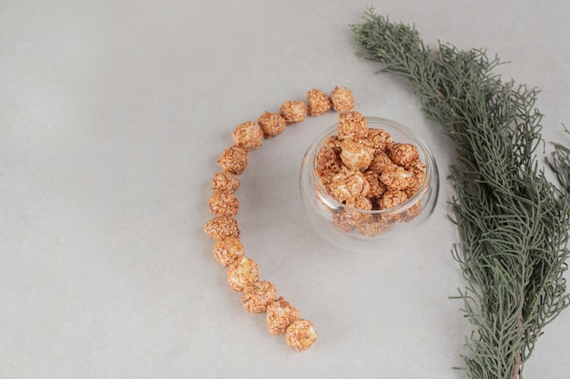 Tree branch next to decoratively aligned mass of popcorn candy on marble table.