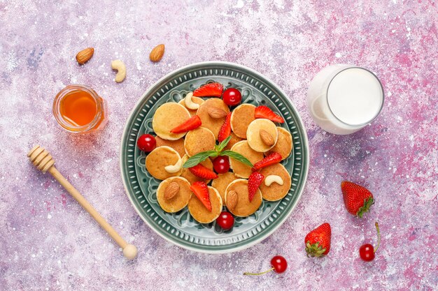 Free photo trendy food - mini pancake cereal. heap of cereal pancakes with berries and nuts.