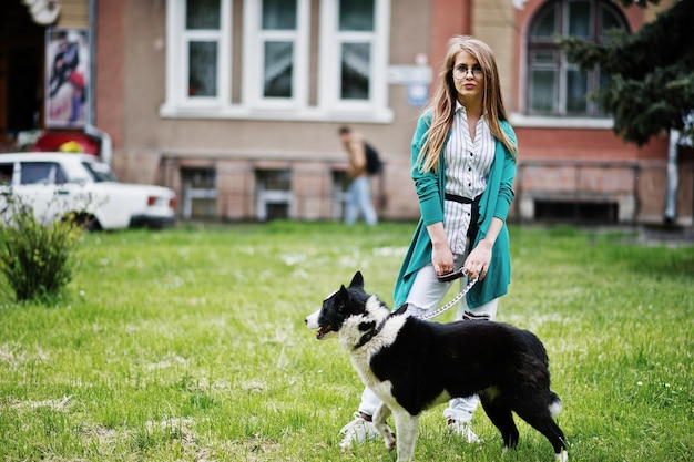 Trendy girl at glasses and ripped jeans with russoeuropean laika husky dog on a leash against street of city Friend human with animal theme