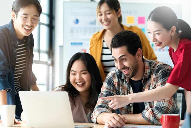 Trendy hipster asian creative friend smiling while sitting at casual meeting with group of friends coworker are working in new success project while using laptop computers digital