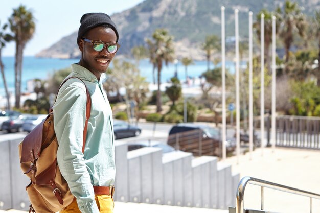 Trendy student in hat and shades enjoying sunny warm weather