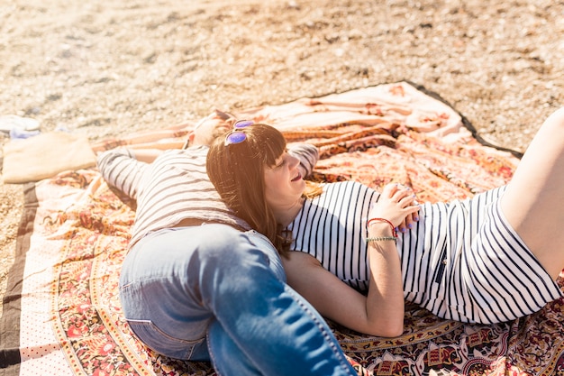 Free photo trendy young couple lying on blanket at beach