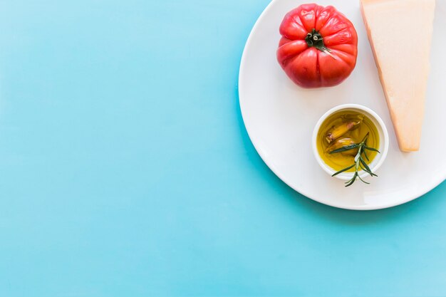 Free photo triangular cheddar cheese with red tomato and garlic glove and rosemary herb oil on plate