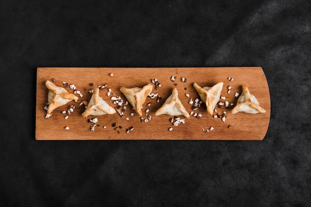 Free photo triangular dumplings on wooden tray over the black background