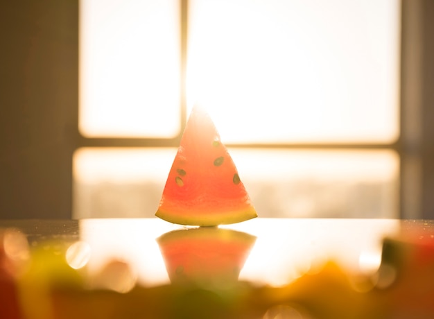 Free Photo triangular shape of watermelon with seeds on reflective desk in bright sunlight