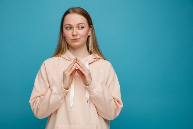 Tricky young blonde woman keeping hands together looking at side 