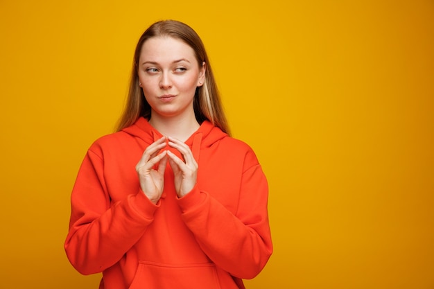 Tricky young blonde woman keeping hands together looking at side 