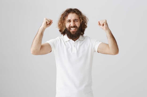 Free photo triumphing happy middle-eastern guy raising hands in yes gesture, celebrating victory