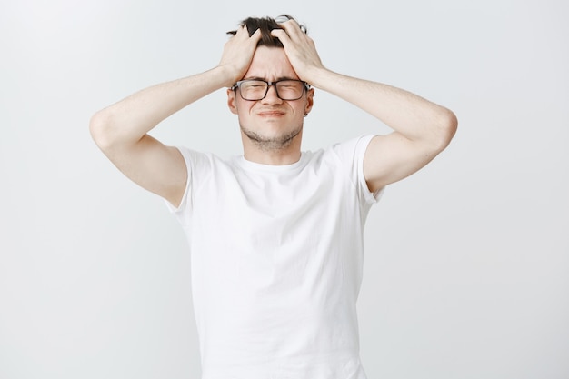 Free Photo troubled and exhausted young man grab head and close eyes from overthinking