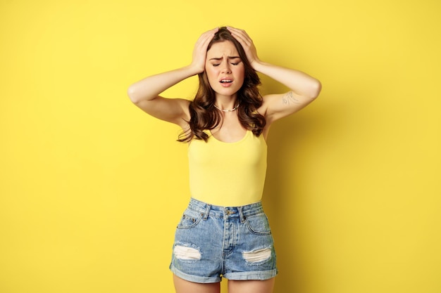 Free Photo troubled and shocked woman holding hands on head, panicking, feeling distressed and anxious, having problem, standing over yellow background