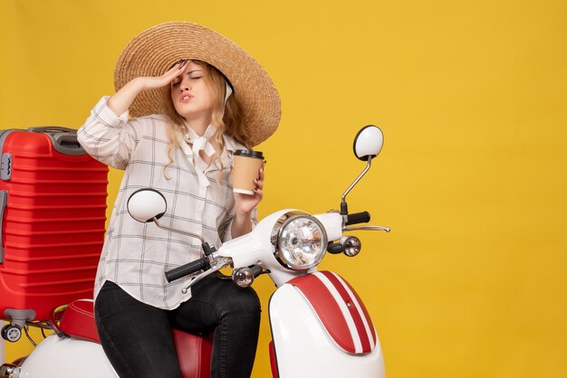 Troubled young woman wearing hat and suffering from headache sitting on motorcycle and showing ticket