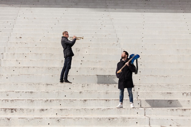 Free photo trumpet player and guitarist on concrete stairs