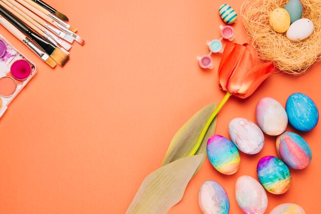 Tulip flower; paintbrushes; colorful easter eggs and nest on an orange background