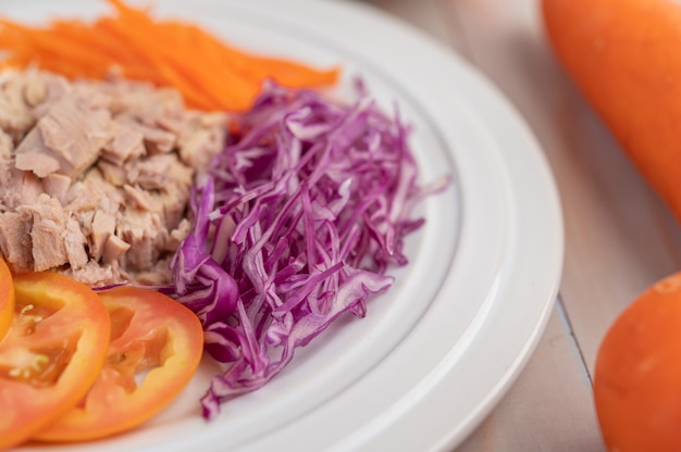 Tuna salad with carrots, tomatoes, cabbage on a white plate on a wooden floor.