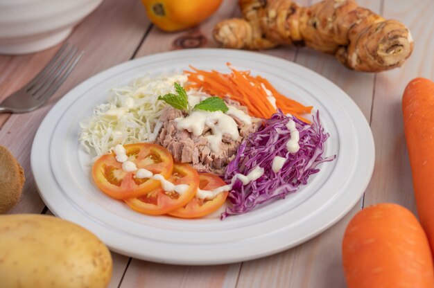 Tuna salad with carrots, tomatoes, cabbage on a white plate on a wooden floor.