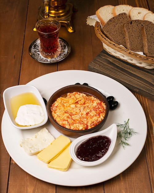 Turkish breakfast menemen with honey, cream, olives, jam and cheese variations in white plate and glass of tea