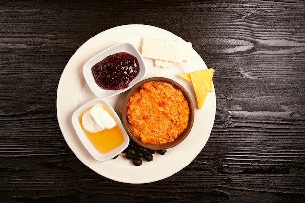 Turkish breakfast menemen with honey, cream, olives, jam and cheese variations in white plate and glass of tea