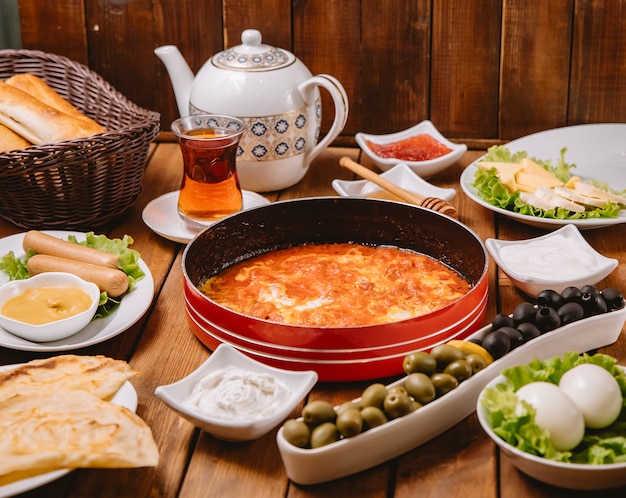 Turkish breakfast setup with egg and tomato dish sausages olives eggs cheese butter and tea